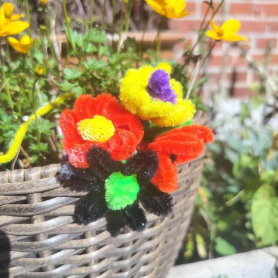 Fire søde blomster skabt af piberensere stukket i en fletkurv med grønne planter.