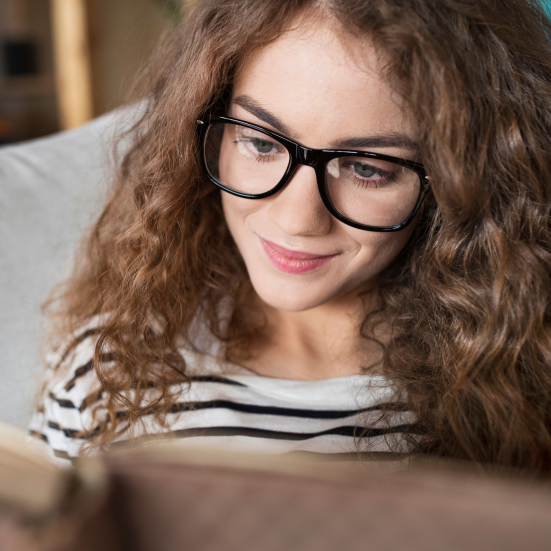 Ung pige med briller læser koncentreret en bog