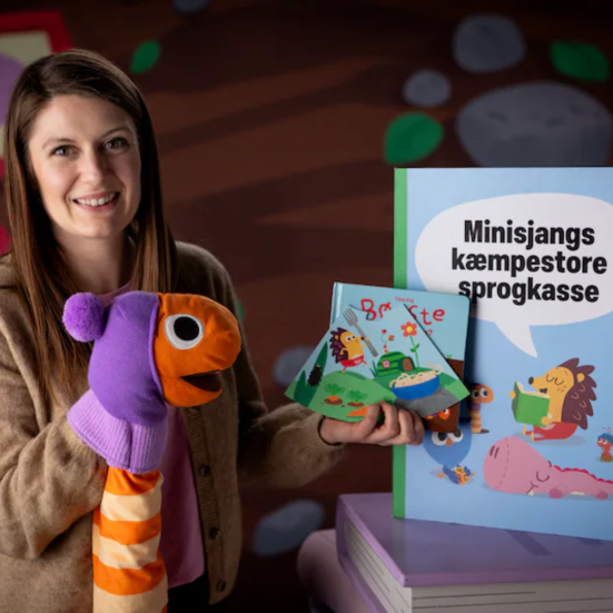 Billede af en dame med en ormedukke på hånden, der viser materialerne fra sprogkassen frem.