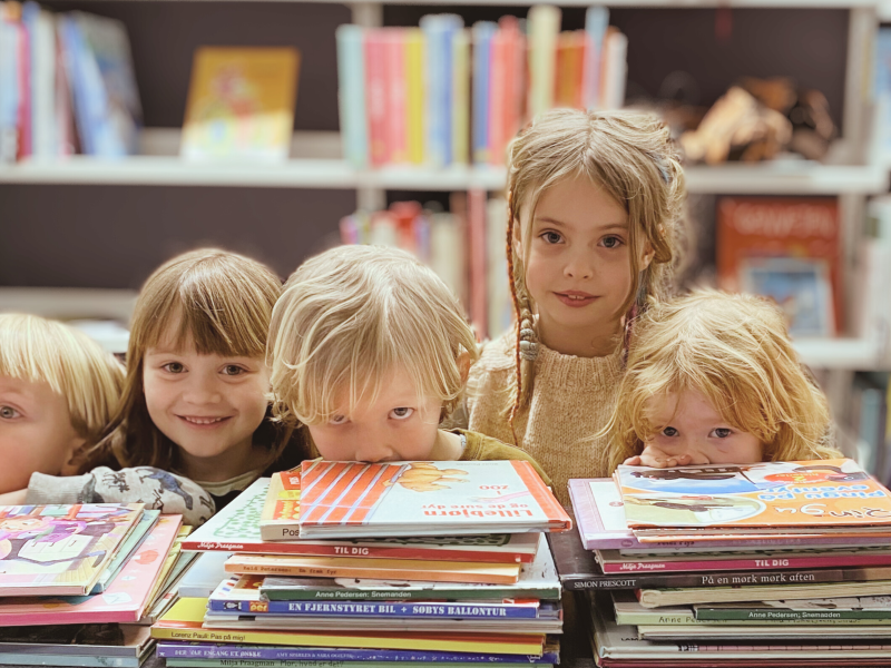 Foto af børn i førskolealderen på besøg på Faaborg Bibliotek. Bogreoler og bogstakke ses for og bag. 