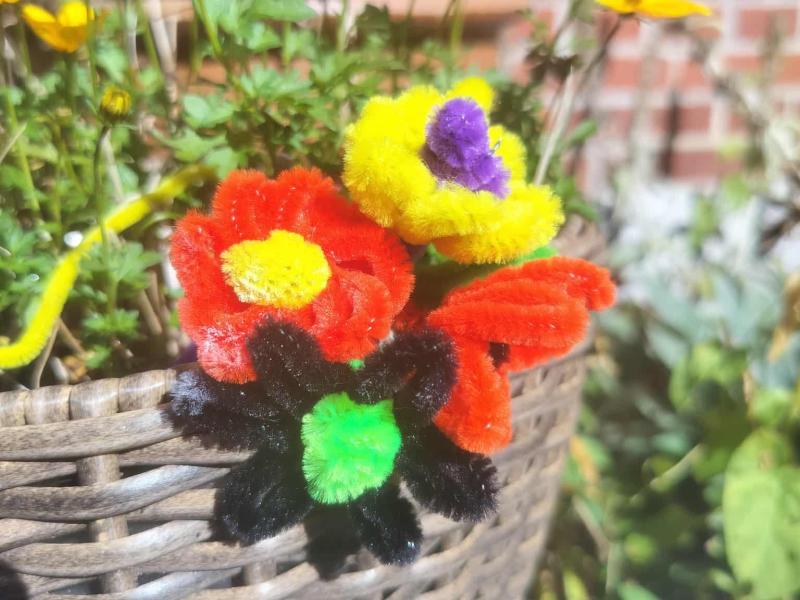 Fire søde blomster skabt af piberensere stukket i en fletkurv med grønne planter.