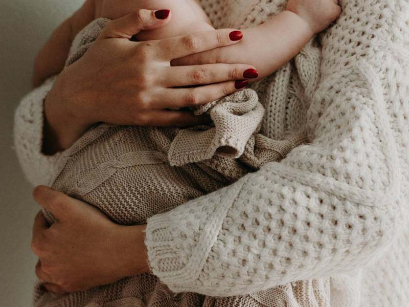 Billede af kvindes torso, holder en baby i armene. 