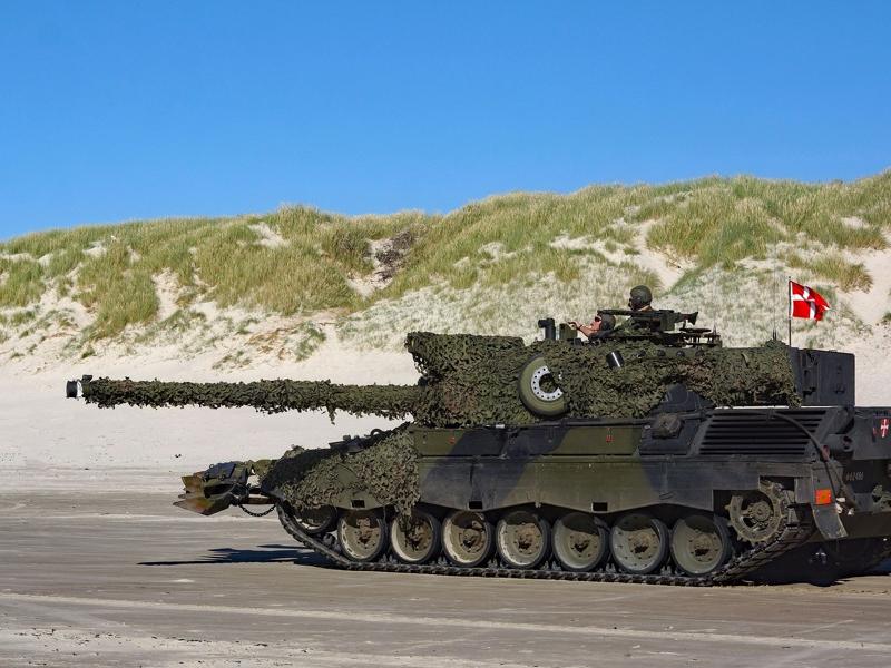Dansk kampvogn på flad strand foran klitter og himmel.