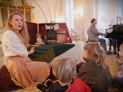 Anne Wæhrens spiller dukketeater for rn gruppe børn og pianist Kristoffer Kaad spille ibaggrunden på et flygel.
