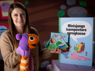 Billede af en dame med en ormedukke på hånden, der viser materialerne fra sprogkassen frem.