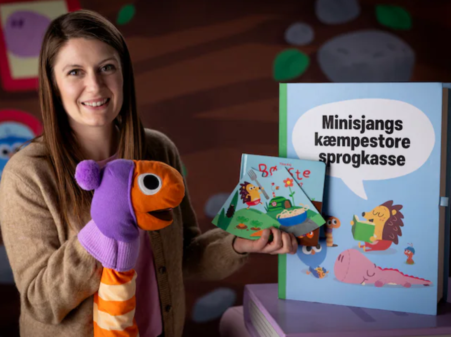 Billede af en dame med en ormedukke på hånden, der viser materialerne fra sprogkassen frem.